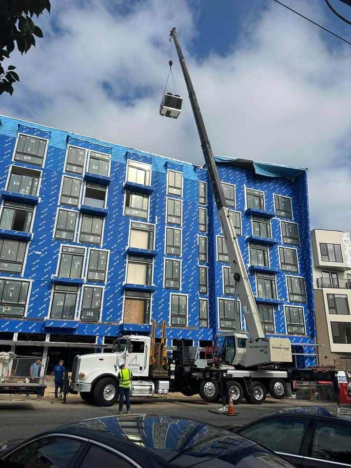 Steedle truck crane setting rooftop HVAC equipment on a multi-story building under construction wrap