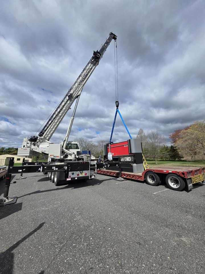 Steedle truck crane lifting industrial machinery from a flatbed trailer into position