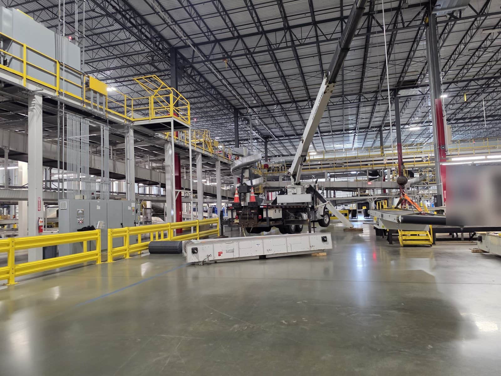 Steedle truck crane set up on the floor of a distribution facility in East Brunswick, NJ with conveyor sections being swapped under the mezzanine
